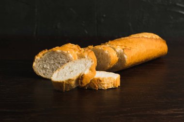 Fragrant fresh French baguette with crust on dark wooden background, side view.