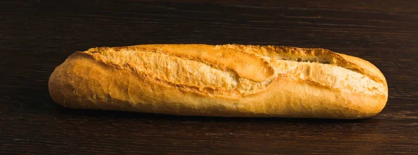 Appetizing french baguette with crust on dark wooden table, background with space for text.