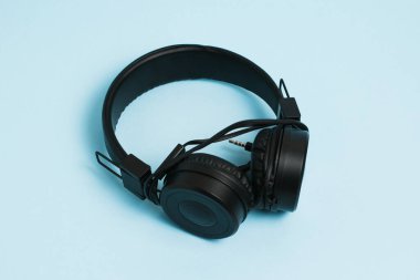 New black headphones with a wire on a light blue paper background