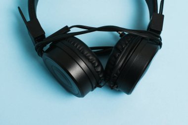 Close-up of new black headphones with wire on light blue paper background.