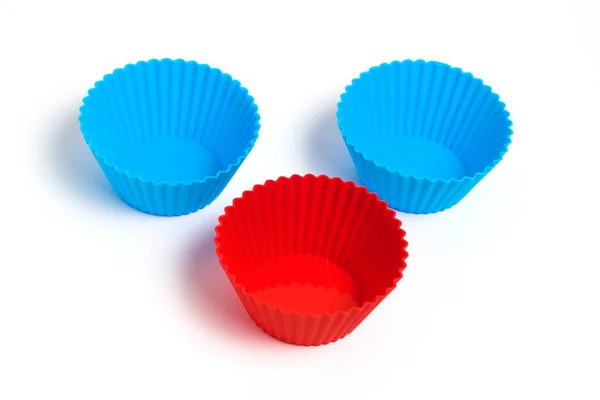Two blue and one red silicone molds for baking a cupcake on a white background.