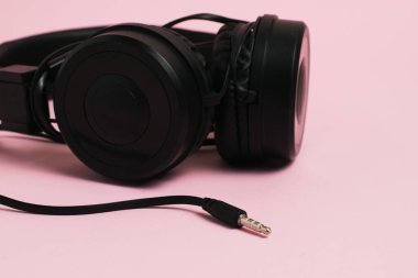 Black stylish headphones with large wire on pink paper background with copy space, headphone jack macro.