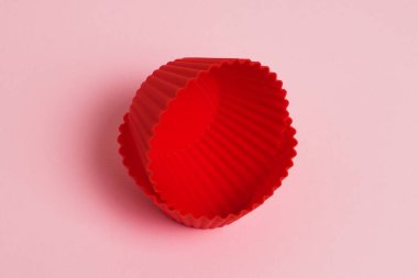 Red silicone molds for cupcakes on a pink paper background.