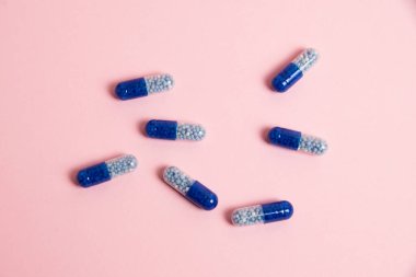 Vitamins in tablet form. Pattern of blue pills on pink paper background with copy space, flat lay