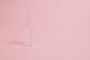 Transparent ampoule with medicine or vitamins on pink paper background with copy space.