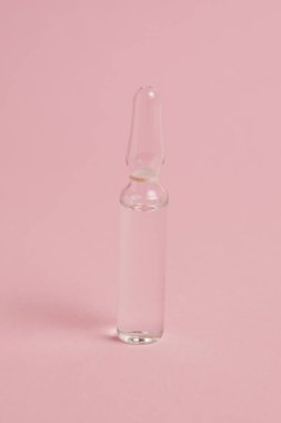 Transparent ampoule with medicine or vitamins on pink paper background with copy space.