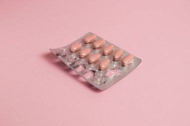 Pink pills in a blister on a pink paper background. Concept of treatment of diseases and support of the body in spring.