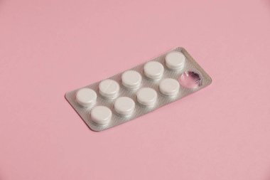 White pills in a blister on a pink paper background. Concept of treatment of diseases and support of the body in spring.