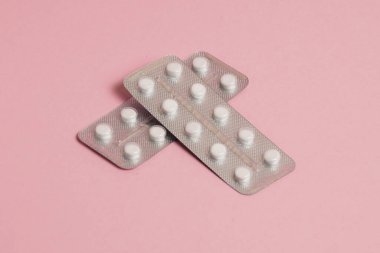 White pills in a blister on a pink paper background. Concept of treatment of diseases and support of the body in spring.