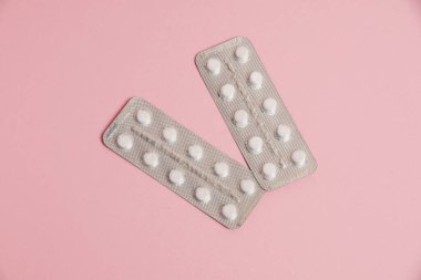 White pills in a blister on a pink paper background. Concept of treatment of diseases and support of the body in spring.