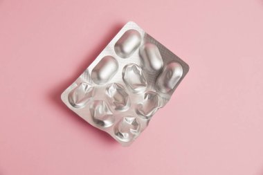 Pills in a gray blister on a pink paper background. Concept of treatment of diseases and support of the body in spring.