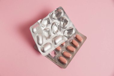 Pills in a gray blister on a pink paper background. Concept of treatment of diseases and support of the body in spring.