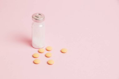 Ampoule and yellow pills on pink paper background with copy space. Concept of treatment of covid 19 and colds