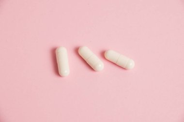 White medical capsules on a pink background with copy space.
