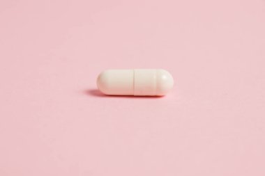 One white medical capsule on a pink background with copy space.