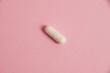 One white medical capsule on a pink background with copy space.