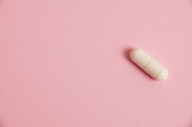 One white medical capsule on a pink background with copy space.