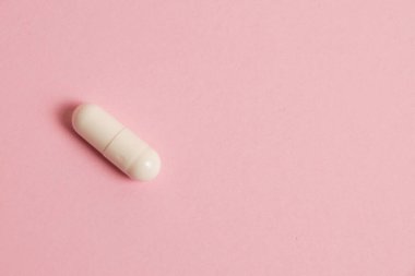One white medical capsule on a pink background with copy space.