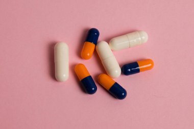 Multicolored medical capsules on pink background with copy space.