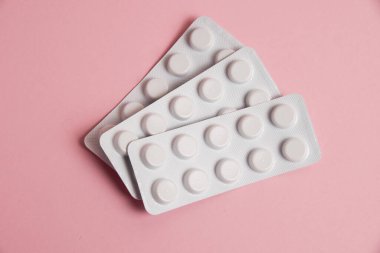 Pills in white blisters on a pink background with copy space, flat lay.