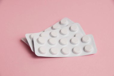 Pills in white blisters on a pink background with copy space