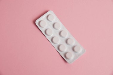 Pills in a white blister on a pink background with copy space, flatlay.