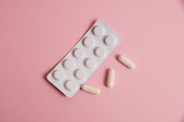 Pills in white blister and medical capsule on pink background with copy space, flatlay.
