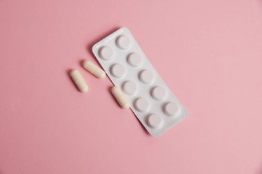 Pills in white blister and medical capsule on pink background with copy space, flatlay.