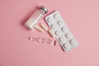 White medical capsules, ampoules with sleeping pill and antibiotic, pills in blister on pink paper background
