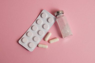 White medical capsules, ampoule and pills in blister pack on pink paper background