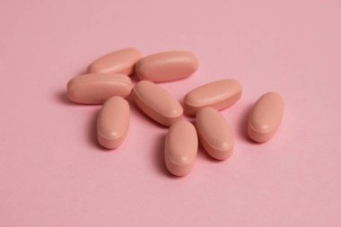 Pink pills on pink paper background with copy space. Concept of taking vitamins in pill form.