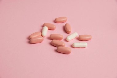 Pink pills and white medical capsules on pink paper background with copy space. The concept of taking vitamins in tablet form.
