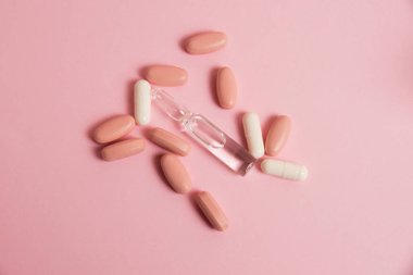 Pink pills, white medical capsules and ampoule on pink paper background with copy space. The concept of taking vitamins in tablet form and in injections.