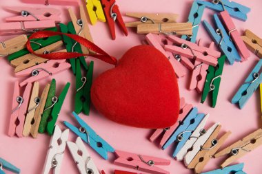 Flatlay, Valentine's Day decor on a paper background. Decorative clothespins and red heart on a pink background