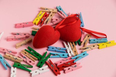 Valentine's day decor on a paper background. Decorative clothespins and red hearts on a pink background