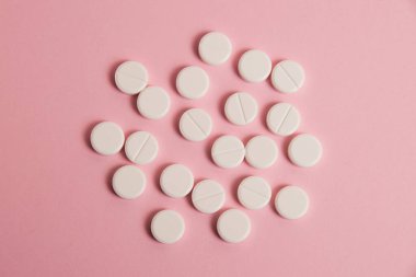 Flatlay, many white pills on a pink paper background.