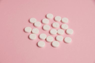 Flatlay, many white pills on a pink paper background.