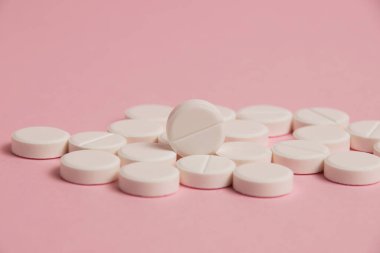 Many white pills macro on pink paper background with space for text.