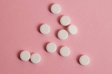 Flatlay, many white pills on a pink paper background.