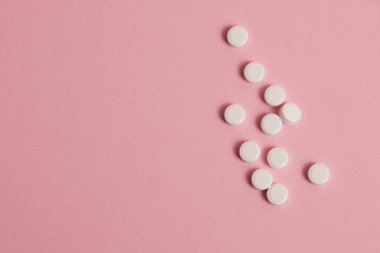 Flatlay, many white pills on a pink paper background.
