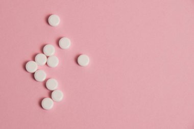 Flatlay, many white pills on a pink paper background.