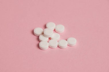 Many white pills on pink paper background with copy space.