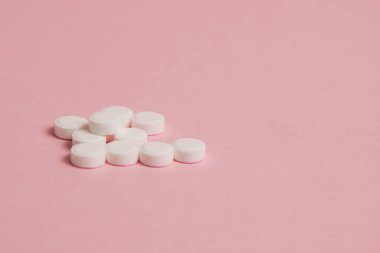 Many white pills on pink paper background with copy space.