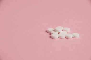Many white pills on pink paper background with copy space.