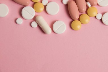 Flatlay, many different pills on pink background with space for text below.