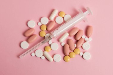 Flatlay, many different pills and a syringe on a pink background.