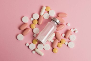 Flatlay, many different pills and an ampoule on a pink background.