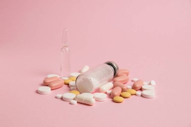 Many different colorful pills on pink paper background, side view.