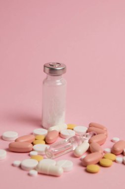 Many different colorful pills on pink paper background, side view, vertical format.