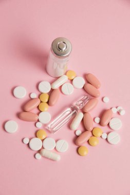 Many different colorful pills on pink paper background, top view, vertical format.